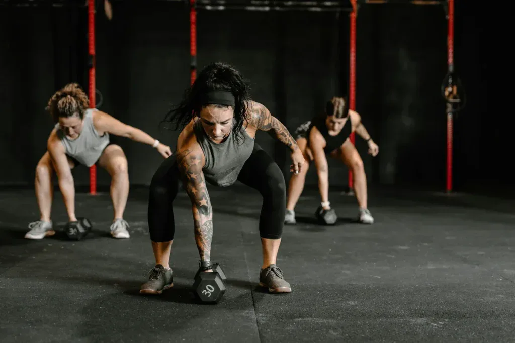 Zajęcia w boxie: trzy zawodniczki w przysiadzie sięgają po hantle w trakcie workoutu