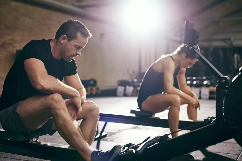 Dwoje zawodników odpoczywa na wioślarzach po skończonym benchmarku CrossFit