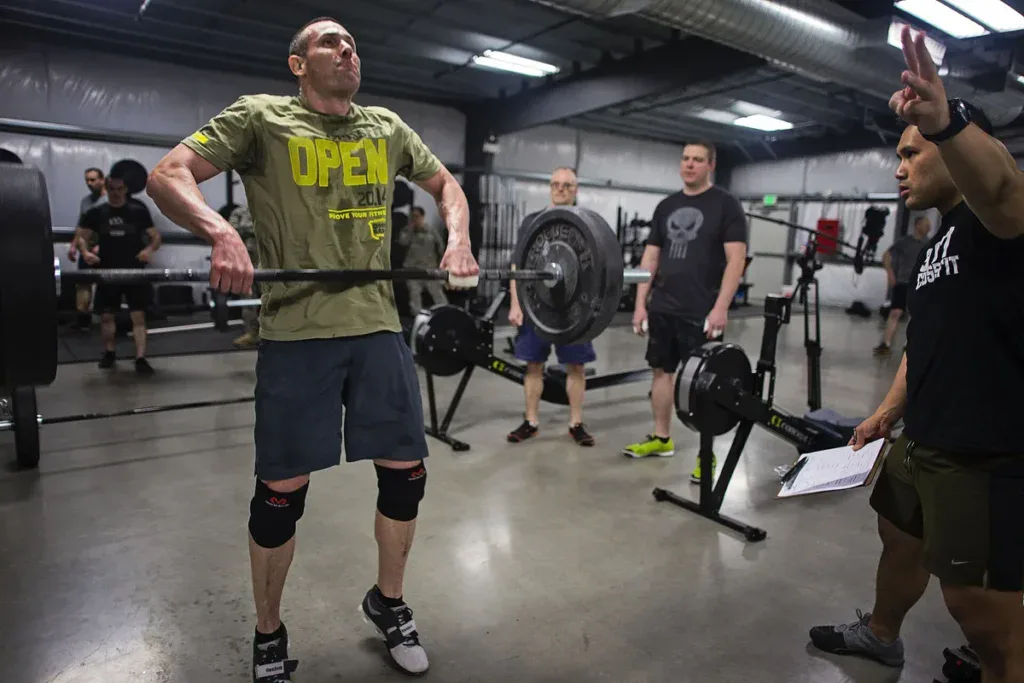 Zawodnik wchodzi pod sztangę w power cleanie podczas CrossFit Open, obok sędzia liczy powtórzenia