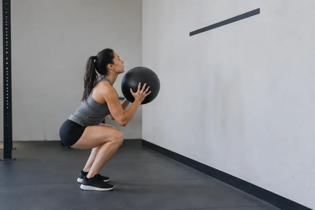 Wall balls: kobieta w dole przysiadu z piłką przy ścianie tuż przed rzutem do celu