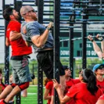 Zawody CrossFit: zawodnicy podciągają się na drążkach, a sędziowie z podkładkami liczą powtórzenia
