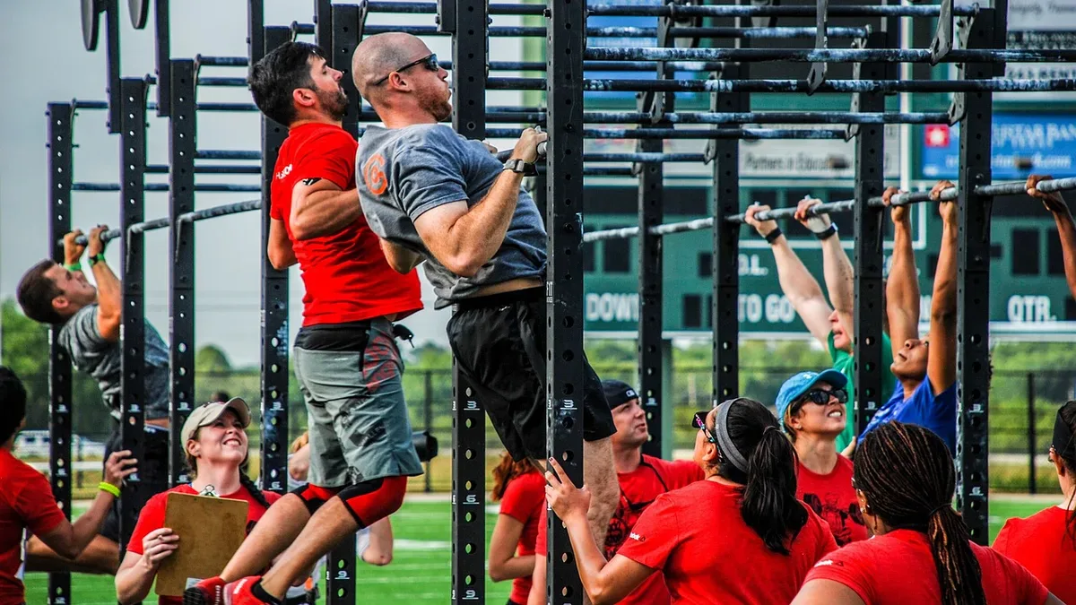 Zawody CrossFit: zawodnicy podciągają się na drążkach, a sędziowie z podkładkami liczą powtórzenia